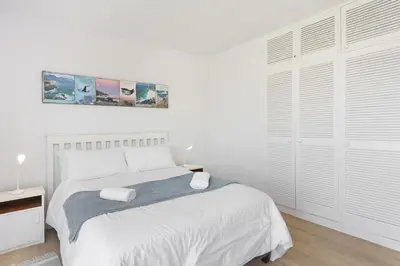 a white bedroom with a bed and a large window at Suidersee-Voelklip in Hermanus