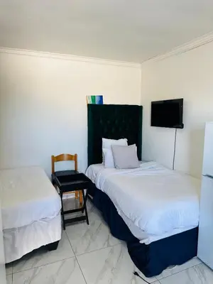 two beds in a room with a chair and a tv at Mila Lodge 2 in Cape Town