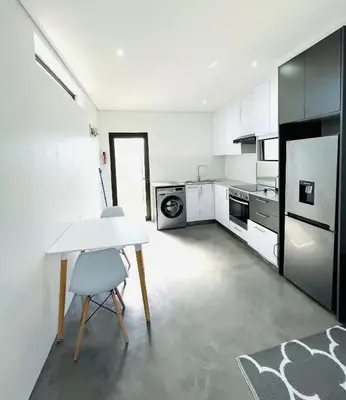 a kitchen with white cabinets and a table and a chair at Sleepy Tides in Cape Town
