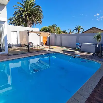 a swimming pool in a backyard with a fence and palm trees at 51 On Vlei in Cape Town