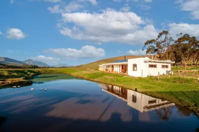 a house on the side of a river with a building at Farmstay at the Goat Shed Cottage, Spinlea Farm in Greyton