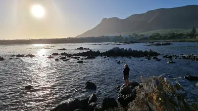a person standing on the rocks near a body of water at The Treehouse Suite in Hermanus