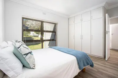 a white bedroom with a bed and a window at Wegbreek in Hermanus