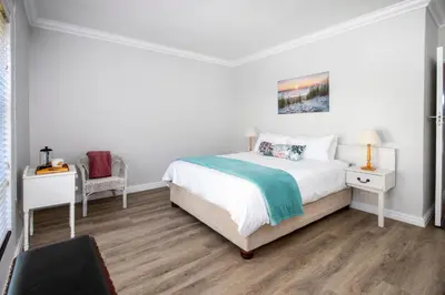 a white bedroom with a bed and a chair at Wegbreek in Hermanus