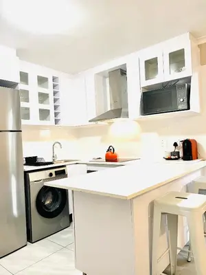 a kitchen with white cabinets and a washer and dryer at Modern charm in Pinelands in Cape Town