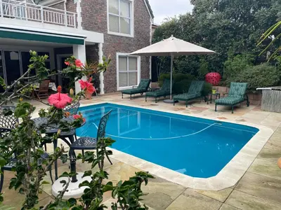 a swimming pool with chairs and an umbrella at De Blauwvoet - Dolfyn (Sunset Beach) in Cape Town