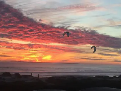 two people flying kites on the beach at sunset at Dolphin Beach beachfront apartment, 3 bedroom-6 persons in Cape Town