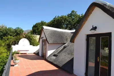a small house with a thatched roof and a patio at Petite France:luxury thatched 4BRcottage with pool in Franschhoek