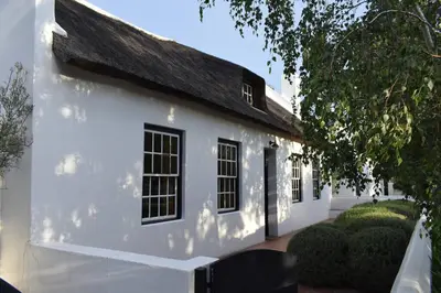 a white house with a black roof at Petite France:luxury thatched 4BRcottage with pool in Franschhoek