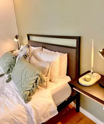 a bed with pillows and a table with a lamp at Petit Casa Central Stellenbosch in Stellenbosch