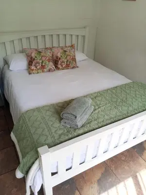 a white bed with a green blanket and pillows on it at Streams Cottage in Bettyʼs Bay
