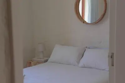 a bedroom with a bed with white sheets and a mirror at Three Streams Cottages in Franschhoek
