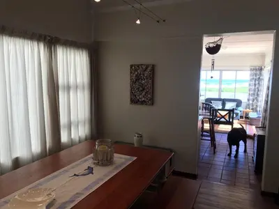 a living room with a dining room table and a dog at La Mer, a beautiful beachfront home in Sandbaai in Hermanus