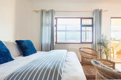 a bedroom with a bed with two chairs and a window at Innie Baai Beach House in Cape Town
